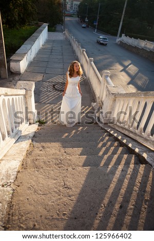 Beautiful bride in a white dress stepping up the concrete steps morning in the sunny city. Outdoors