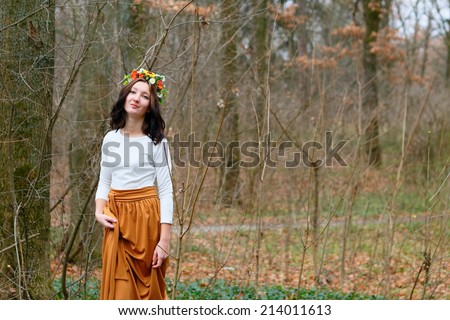 Beautiful girl with flower wreath on her head and orange skirt in the autumn forest