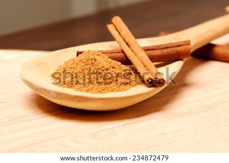 Three cinnamon sticks on a plank and cinnamon powder on a wooden spoon