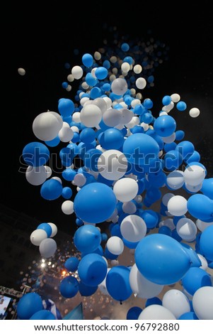 Greece is celebrating, blue and white balloons flying up in the dark sky.