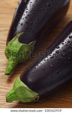 Photo of two eggplants with water droplets on a wood table.