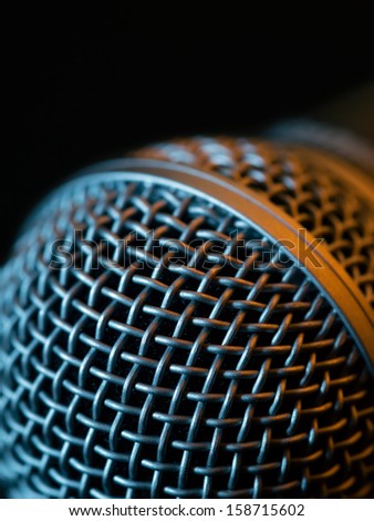 Macro photo of a vocal microphone in low light lit with stage lights.