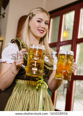Photo of a beautiful female waitress wearing traditional dirndl and holding huge beers in a pub.