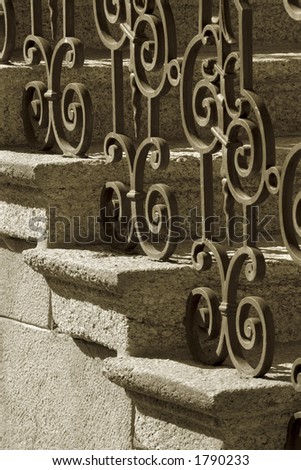 A sepia image of wrought iron handrail and stone steps.