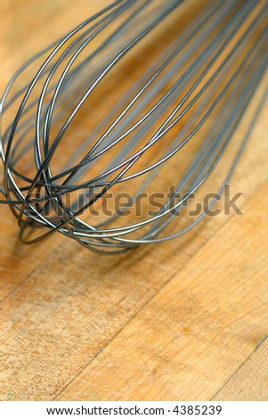 Wire whisk resting on a well worn cutting board of a commercial bakery.  Shallow depth of field.