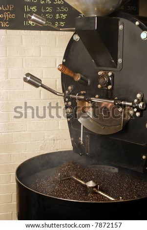 The freshly roasted beans from a large coffee roaster, just as the beans are stirred in the cooling cylinder. Smoke rises while the dark roasted beans are stirred.