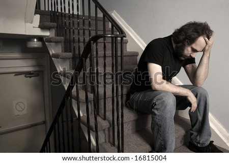 A male adult with overwhelming depression sitting in the stairwell of his apartment building.  Desaturated.