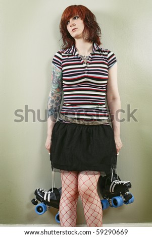 Photograph of a bored roller derby girl holding her skates and waiting against a wall.