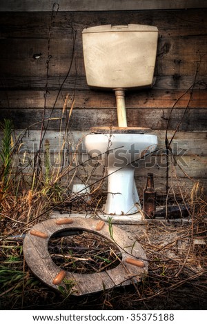 Photo of an old broken toilet cabin surrounded with wild vegetation