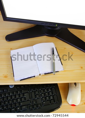 Computer desk with monitor, keyboard, mouse and an opened notebook and pen