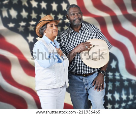 A mature western couple giving tribute to their country.  They\'re against a backdrop of a large American flag.