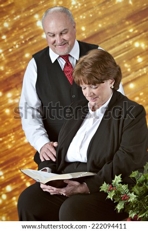 A senior couple reading the Bible together before a bank of diagonal gold lights with holly in the foreground.