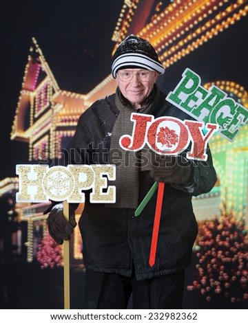 A senior man happily planting Christmas yard signs in front of his decorated house at night.