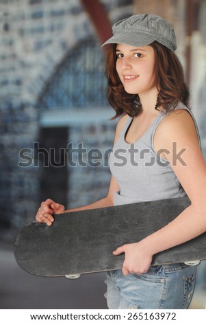A pretty teen girl looking at the viewer as she carries her skateboard past buildings.
