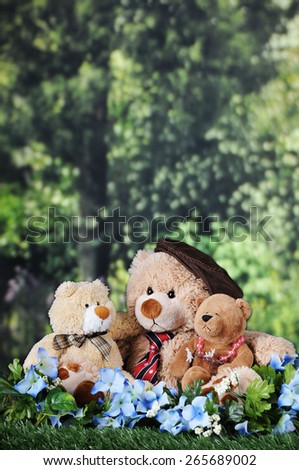Three toy bears -- a papa, son and daughter bear, cuddled together on a lawn near the woods, with room for your text in the trees above and behind.