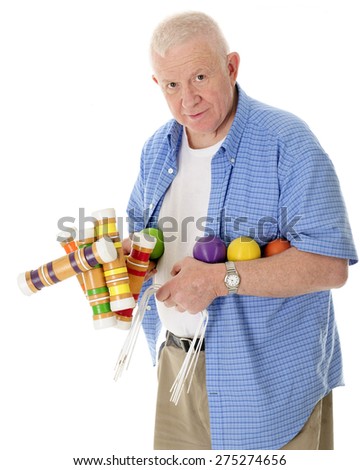 A casual senior adult man looking at the viewer carrying a load of croquet mallets, balls and wickets.  On a white background.