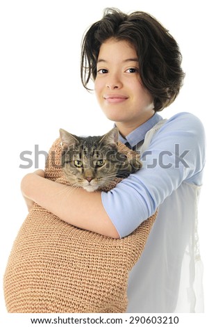 A young teen girl happily holding her pet Tabby cat in a tan, woven shoulder bag.  On a white background.