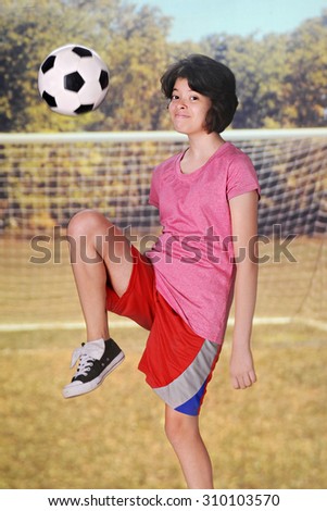 A young teen girl happily kneeing a soccer ball outside on the soccer field.  Motion blur on the ball.