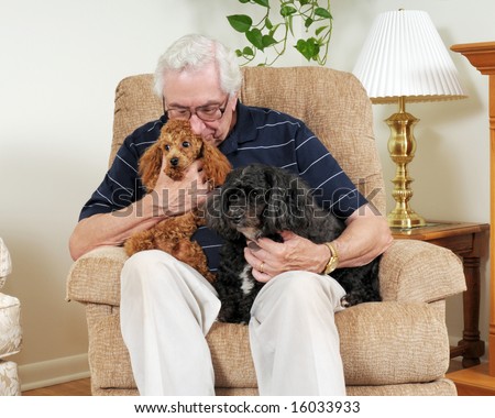 A senior man with two dogs, cuddling with one of them in his living room.