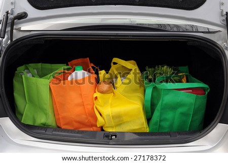 Four colorful eco-friendly shopping bags filled mostly with groceries in the trunk of a car.