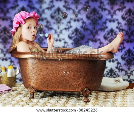 A beautiful preschooler blowing bubbles while wearing a bath bonnet in an old-time copper tub.