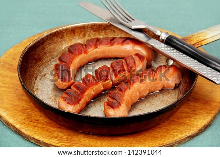 three grilled sausages on a metal pan, lower, fork, round wooden cutting board.