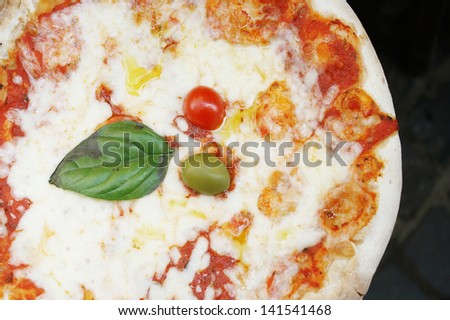Detail of a delicious pizza pie with a basil leaves, an olive and a fresh tomato as a decoration