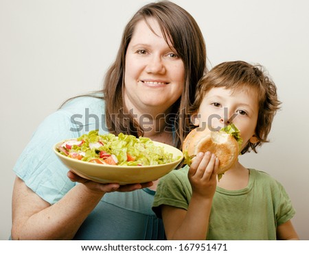 fat woman holding salad and little cute boy with hamburger teasing