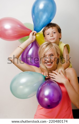 pretty family with color balloons on white background, blond woman with little boy at birthday party