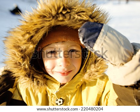 little cute boy in hood with fur on snow outside, sunny smiling