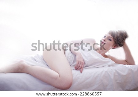 pretty blond woman laying in bed on white shits