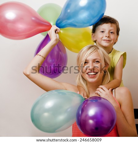 pretty real family with color balloons on white background, blond woman with little boy on birthday party isolated