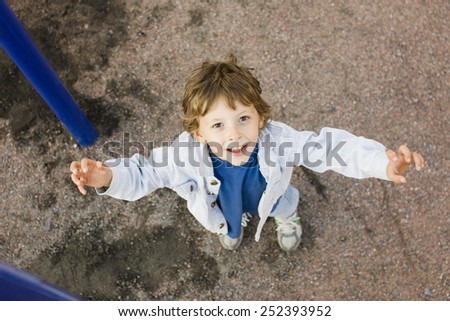 little cute boy playing on playground, hanging on gymnastic ring smiling, hands up