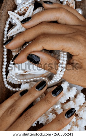 close up nails with manicure among sea stuff, shell, coral, starfish, african tanned hands