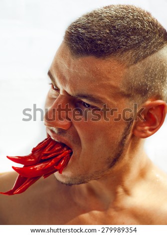 desperate young man with a lot of chilli pepper in mouth, looking angry dragon with flame, burning agony