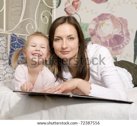 portrait of mother and daughter laying in bed  reading book and talking