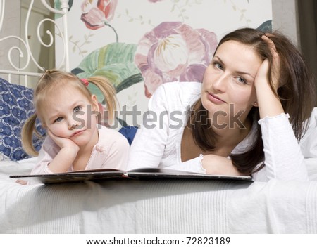 portrait of happy family, mother and daughter in bed reading book and talking, laughing