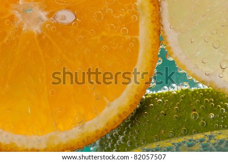 Three slices of fruit - an orange, a lemon and a lime - in soda water  against an ultramarine blue background