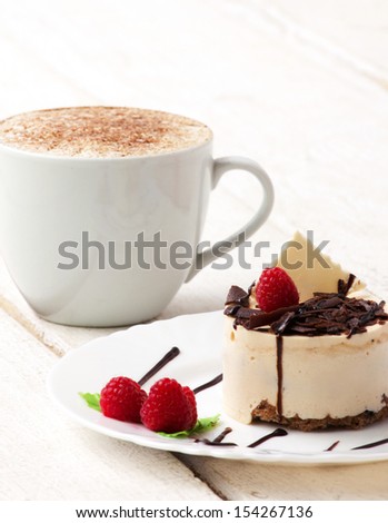 coffee with cream and cup-cake with raspberry and chocolate in white plate on wooden white table