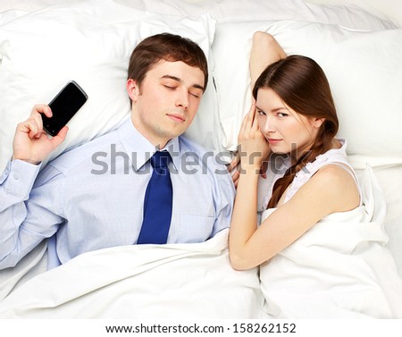 man obsessed by work sleeping in bed with beautiful woman
