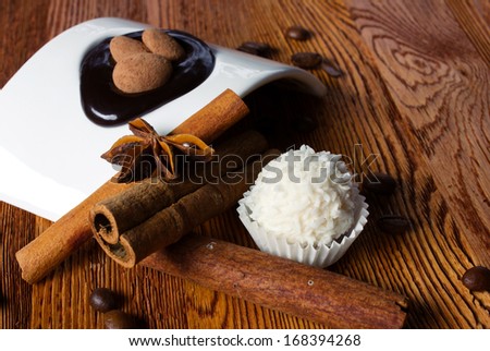 tasty still - white candy with coconut flakes, sticks of cinnamon, anise and white modern plate with brown ball candy on wooden table