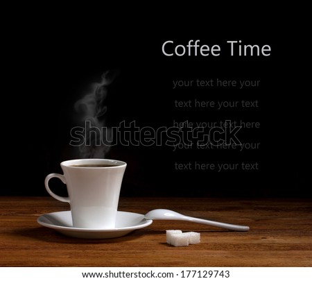 white ceramic cup with hot coffee  on saucer, ceramic spoon and lumps sugar on wooden table on dark background