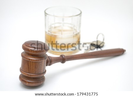 A courtroom gavel with a deliberately blurred background of highball glass and hard liquor with ice cube, and keys