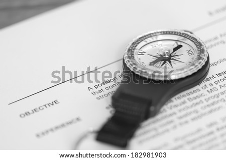 A compass sits on a job resume, indicating career direction; extremely shallow depth of field to emphasize employment on the resume and direction