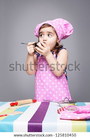 little cute chef tasting her food on grey background