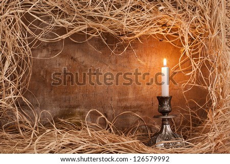 single candle burning on candle holder on grunge wooden background with straws