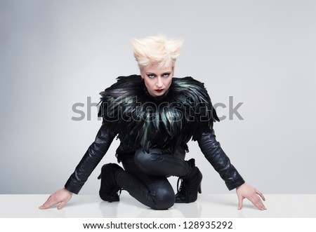 young model with crazy hair and leather clothes posing and looking at camera on a white platform with grey background