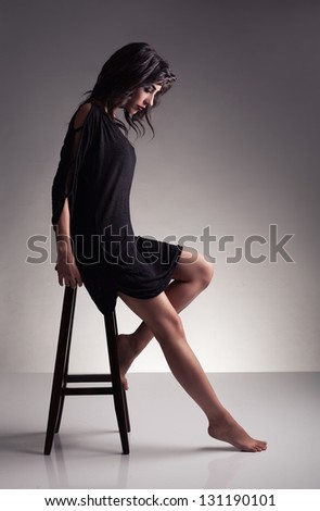 profile of a young brunette model with barefoot looking down on grey background