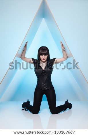 young beautiful woman in a futuristic costume posing on a triangle platform on blue background