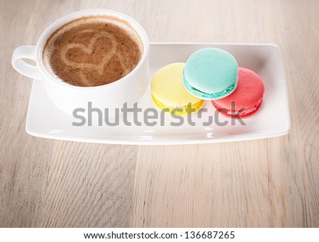 cup of coffee and colorful macaroons on a porcelain plate on wooden table